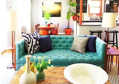 Turquoise blue tufted tuxedo sofa in a designer living room with pops of navy and natural woods and textures